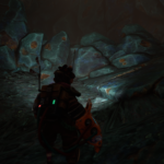 A character in The Gunk explores a dimly lit cave with large, textured rocks.